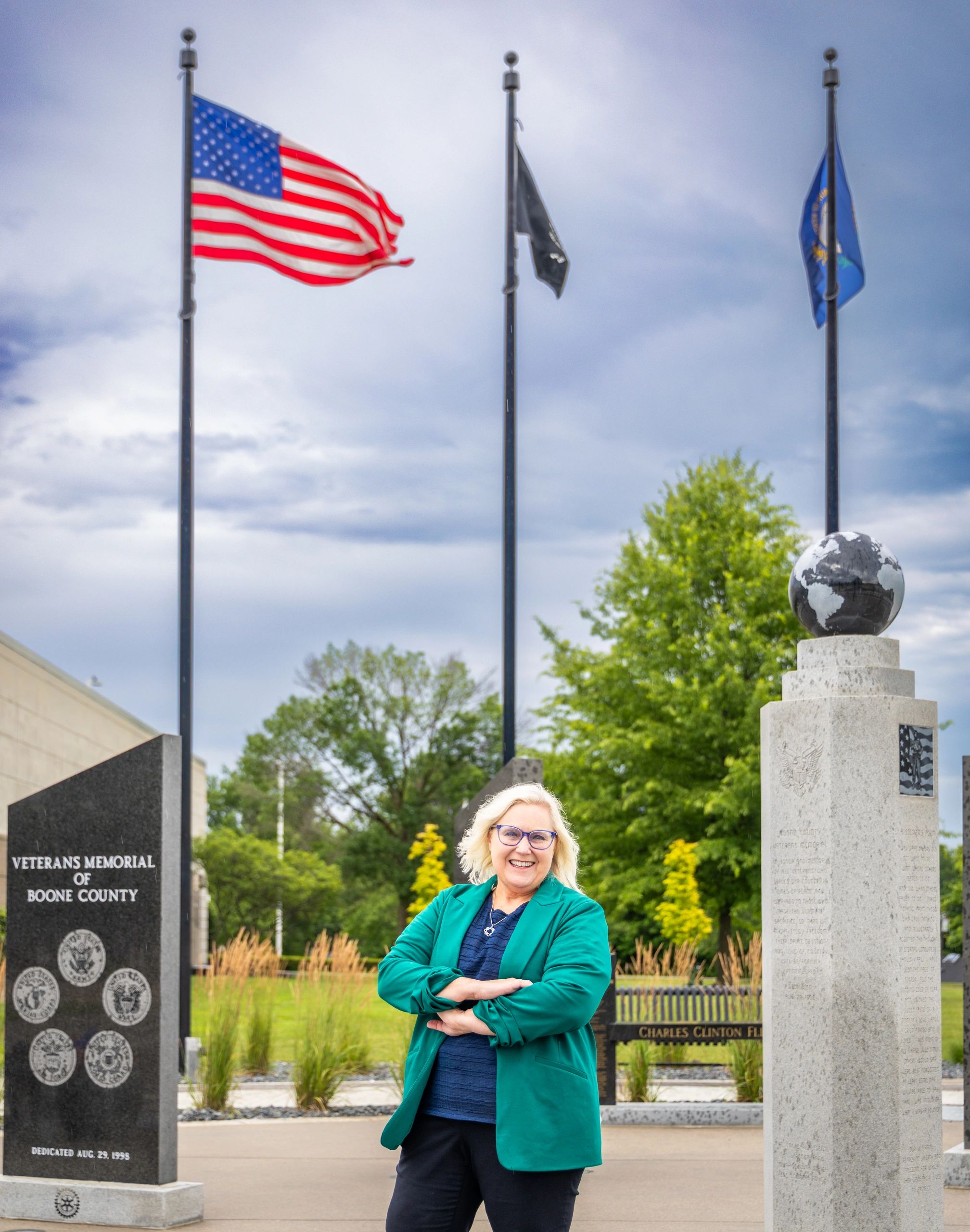 Smiling woman in green blazer at veterans memorial.