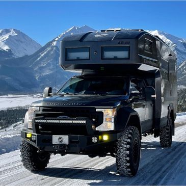 Black off-road camper truck on snowy mountain road.