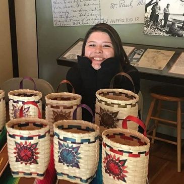 Smiling woman showcases handcrafted woven baskets at a Minnesota Historical Society exhibit.