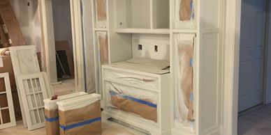 A room with built-in cabinetry under renovation, with parts masked for painting.