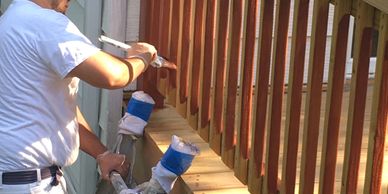Man painting wooden railing on a porch in sunlight.