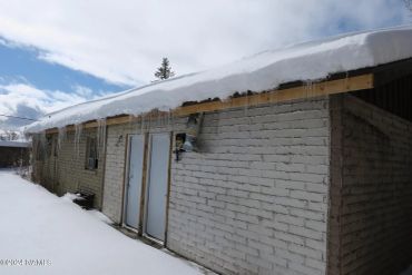 Snow-covered roof on a brick building under a partly cloudy sky.