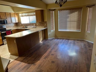 Empty kitchen and dining area with wood floors and blinds.