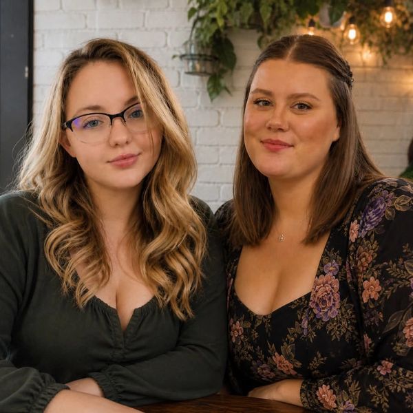 Two women sitting closely together, smiling gently at the camera indoors.
