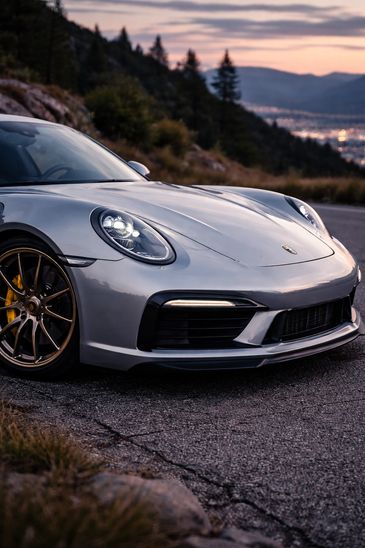 Close-up of a sleek silver Porsche sports car on a scenic mountain road.