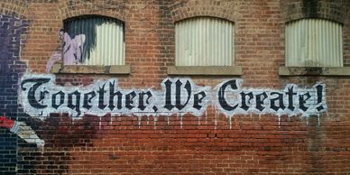Brick building with painted graffiti that states “Together, we create!”  