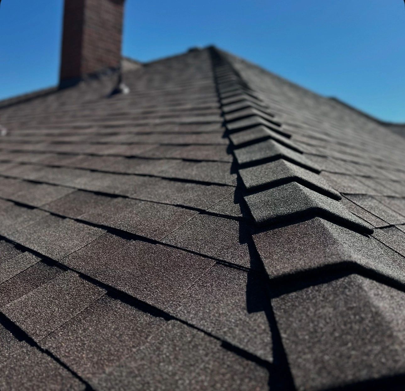 Close-up of a dark shingle roof under clear blue sky.