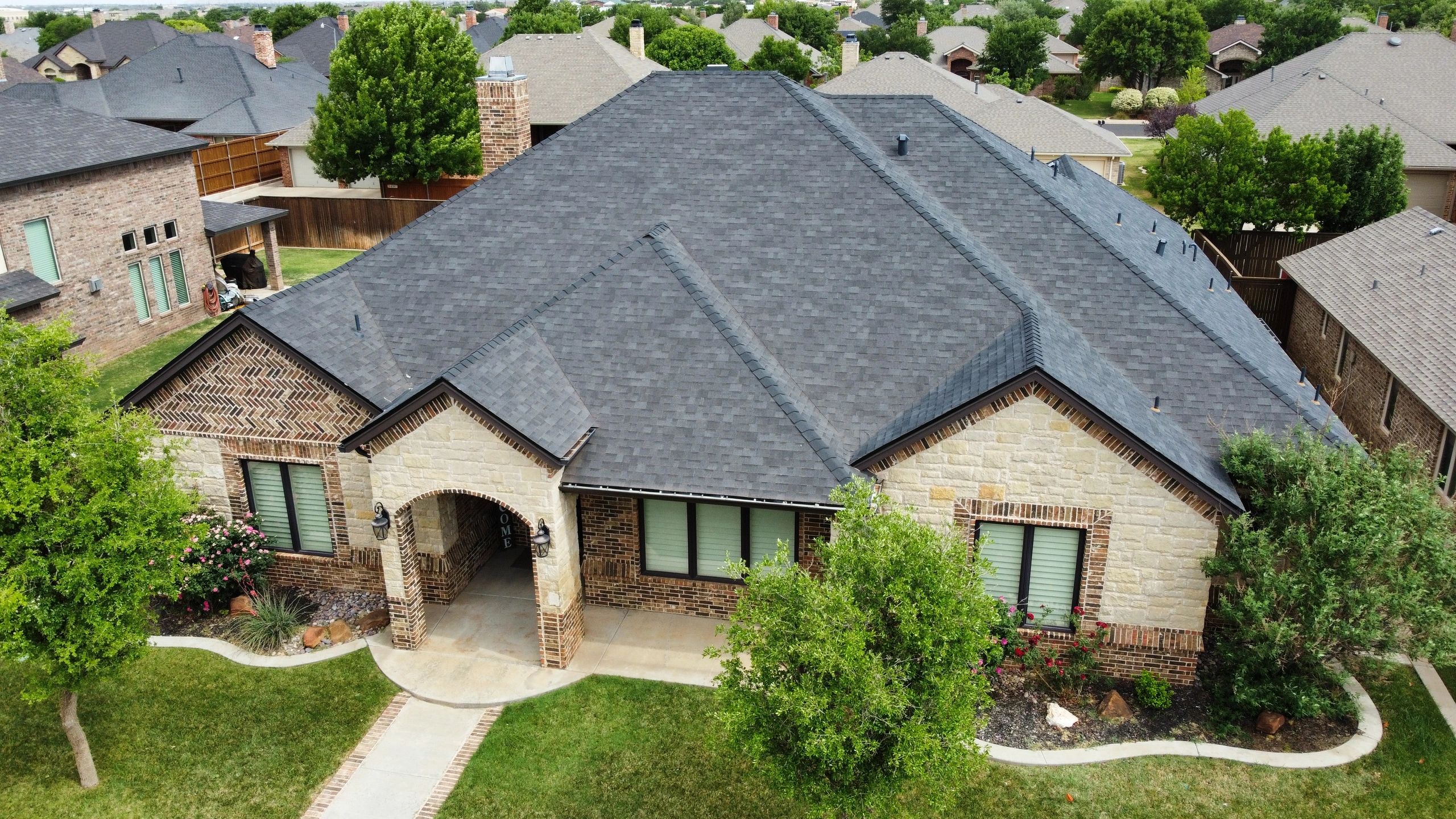 A suburban brick house with a dark gray shingled roof and landscaped yard.