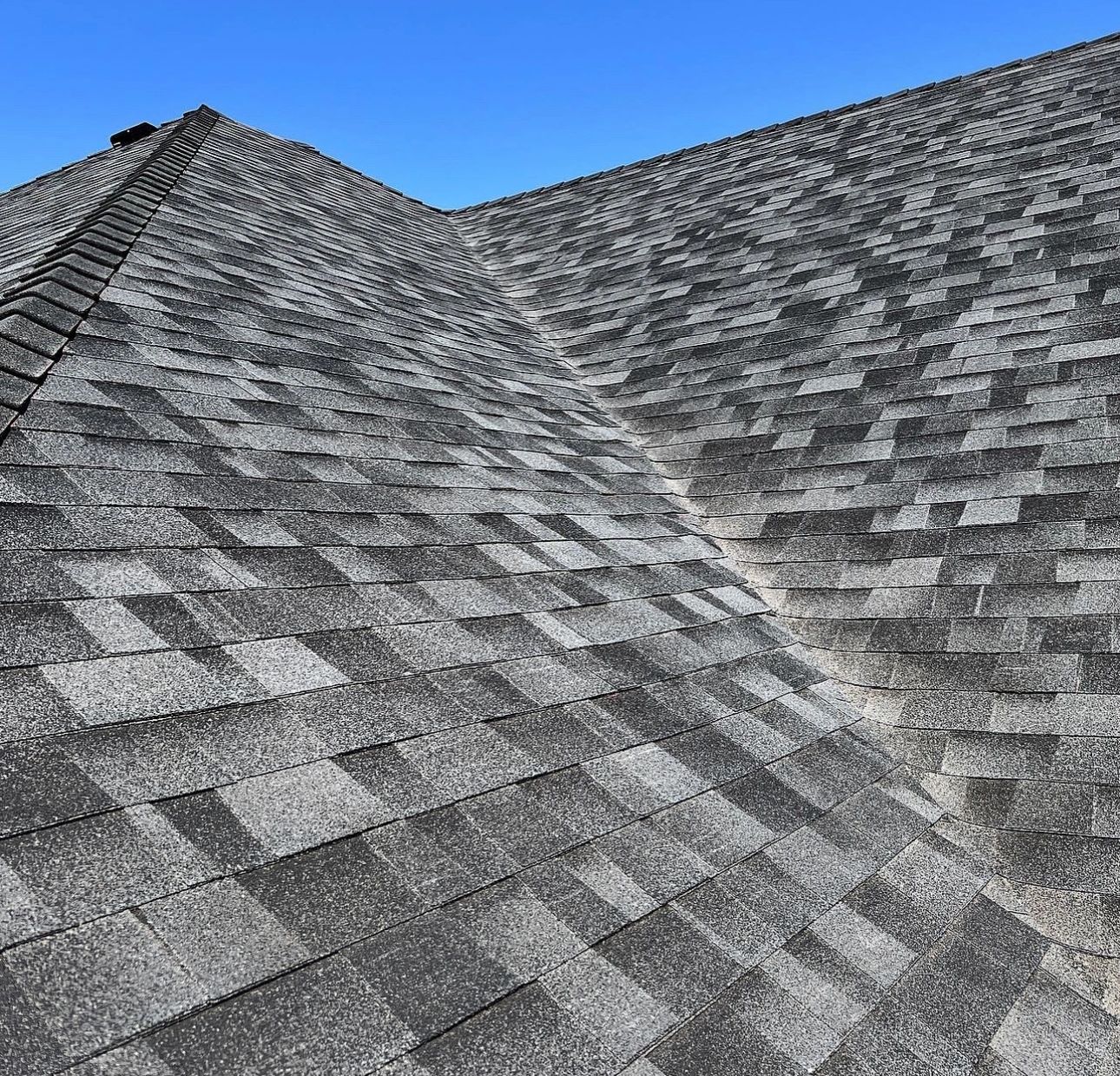 Close-up of a gray shingle roof against a clear blue sky.
