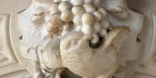 Detailed marble carving of a bird with grapes and leaves.