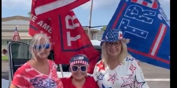 Three women dressed in patriotic clothing with Trump flags.