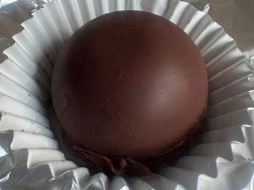 Round chocolate dessert in a white paper cup.