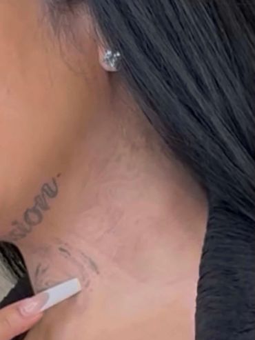 Close-up of a woman's neck with faded tattoos and a diamond stud earring.