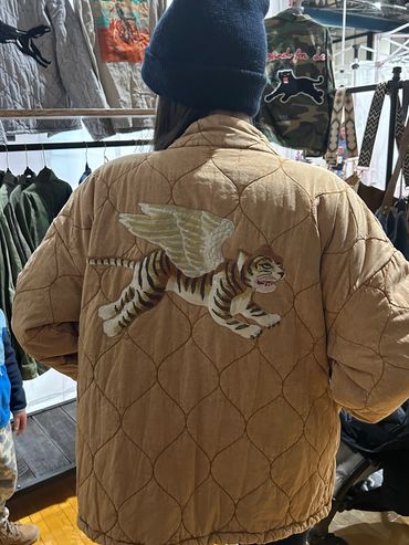 Person wearing a tan quilted jacket with a winged tiger design on the back.