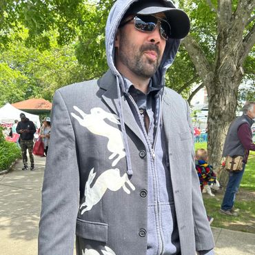 Man wearing a gray blazer with white rabbit designs and sunglasses outdoors.