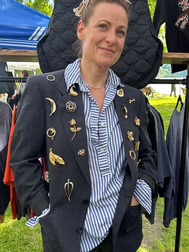 Woman wearing a striped shirt and a blazer decorated with various pins and brooches.