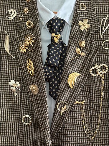 Houndstooth jacket adorned with various gold brooches and a patterned tie.