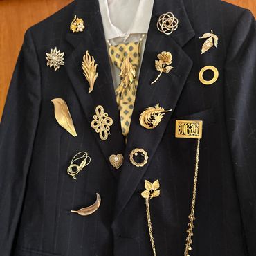 Black blazer adorned with various gold brooches and a polka dot tie.