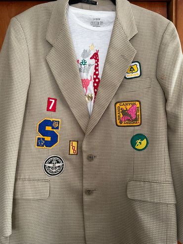 Beige blazer adorned with colorful patches and a giraffe-printed shirt underneath.