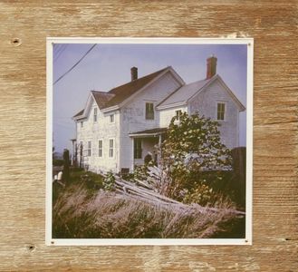 Old white wooden house surrounded by grass and a fence.