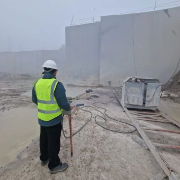 Worker in safety vest and helmet at a dusty site.