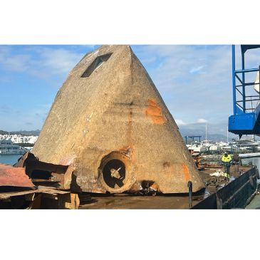 Old, rusty conical metal structure near a harbor.