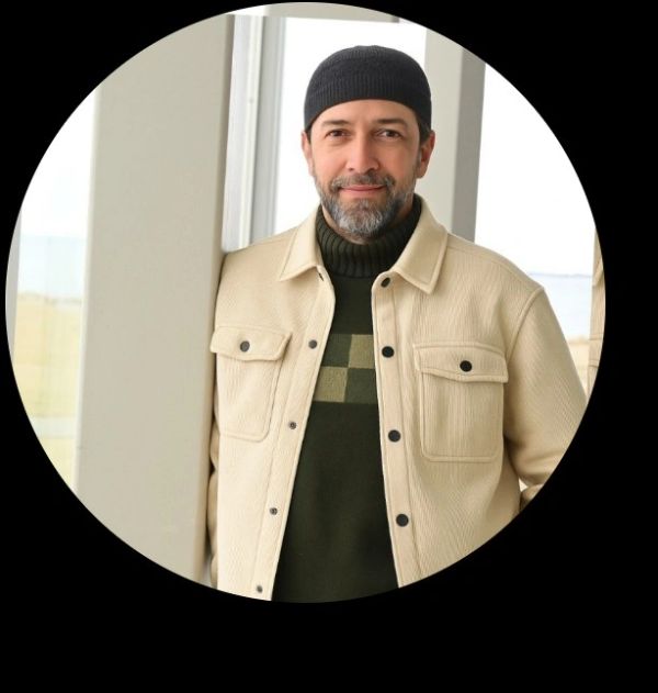 Man in beige jacket and black headwear smiling.