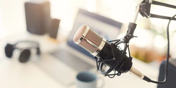 Professional microphone setup with a blurred laptop and headphones in the background.