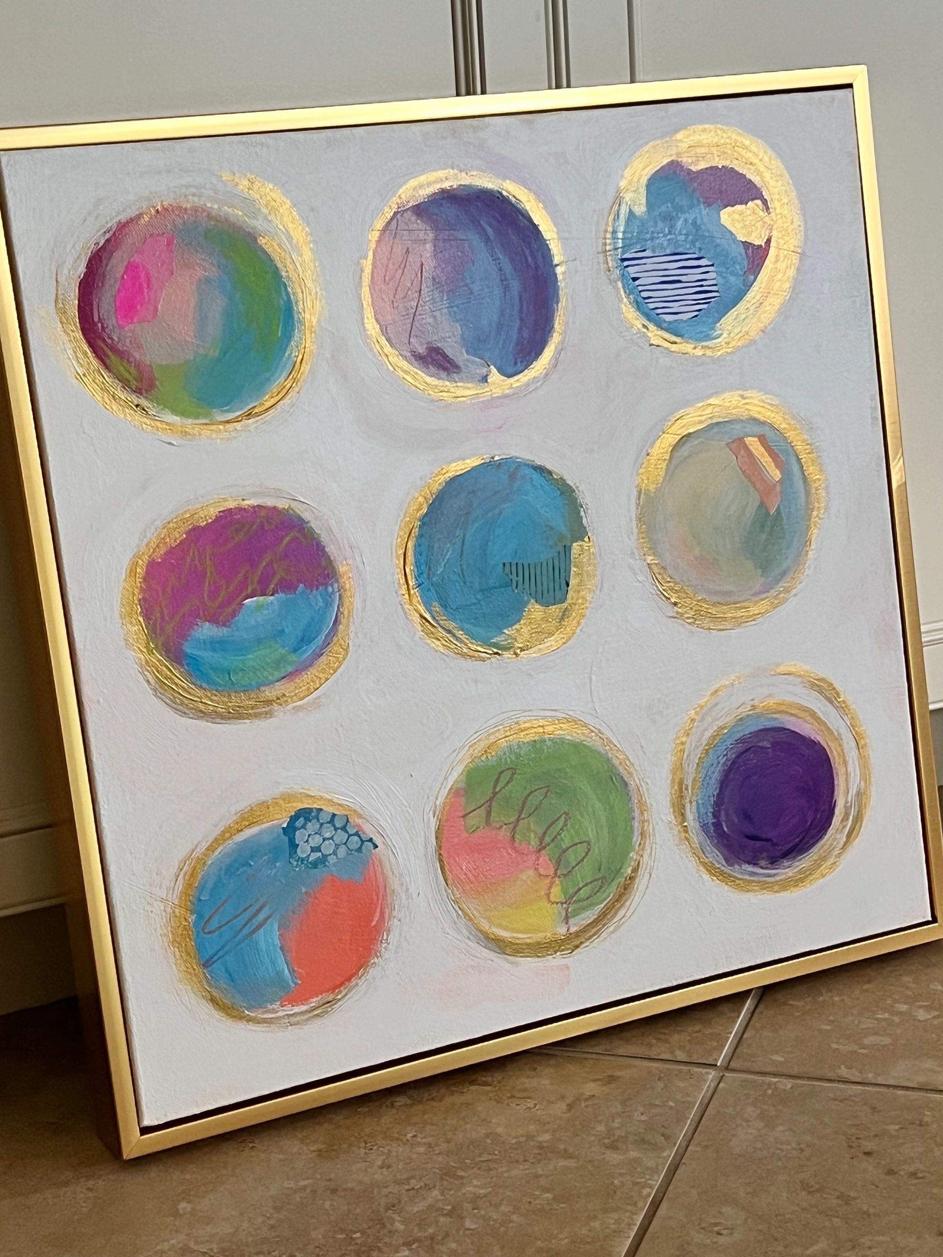 Abstract painting with nine colorful circular shapes framed in gold.