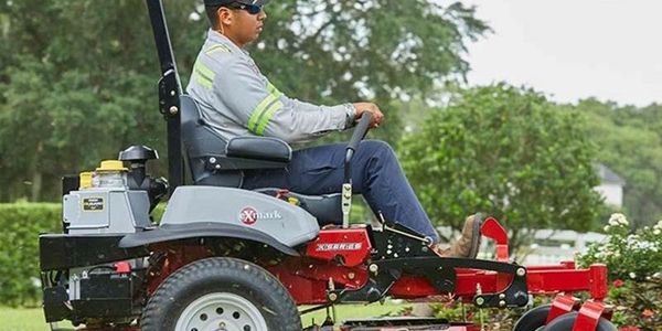 Man operating a red zero-turn lawn mower on grass.