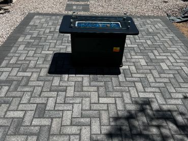 Outdoor black fire pit table on patterned stone patio.