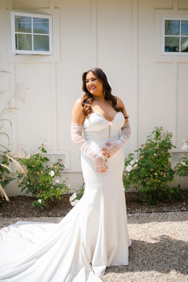 Bride in a white wedding dress smiling outdoors.
