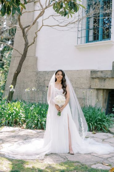 Bride in white wedding dress holding bouquet outdoors.