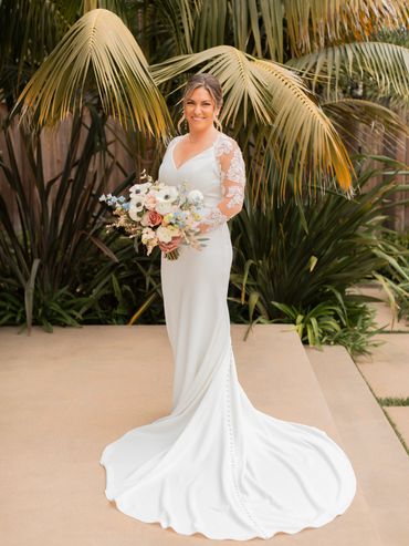 Bride in a white wedding dress holding a bouquet outdoors.
