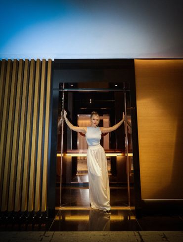 Woman in elegant white dress posing in a stylish, modern doorway with warm lighting.