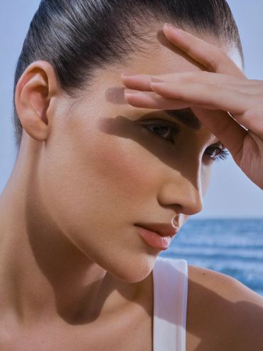 Close-up of a woman shielding her eyes from the sun by the sea.