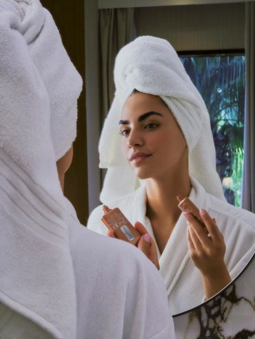 Woman with towel on head holding Clinique products in front of mirror.