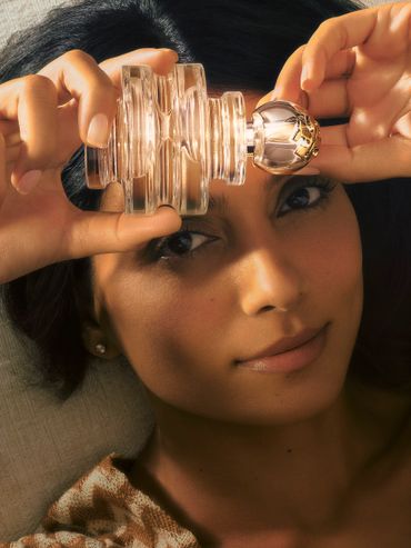 Woman holding an ornate perfume bottle near her face.