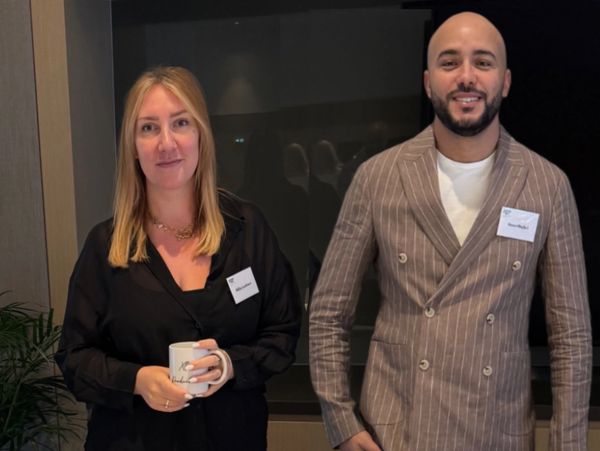 Two professionals posing indoors, one holding a mug.