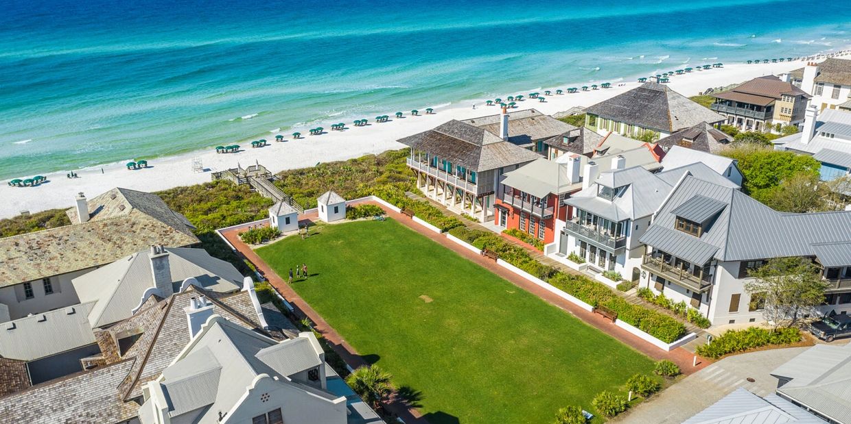 Aerial view of beachfront homes with green lawn and turquoise ocean.