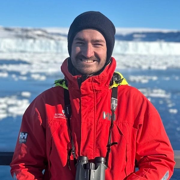 Man smiling in a red winter jacket with binoculars in an icy landscape.