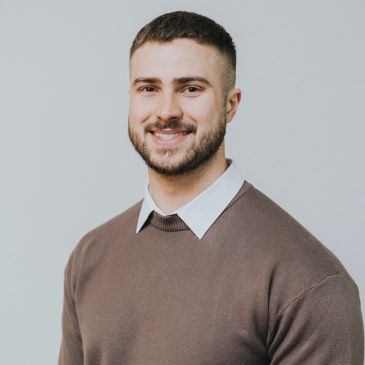 Smiling young man in brown sweater and white shirt.