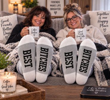 Two friends wearing matching socks that say best bitches, enjoying coffee at home.