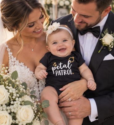 Smiling bride and groom holding a happy baby in a wedding setting.