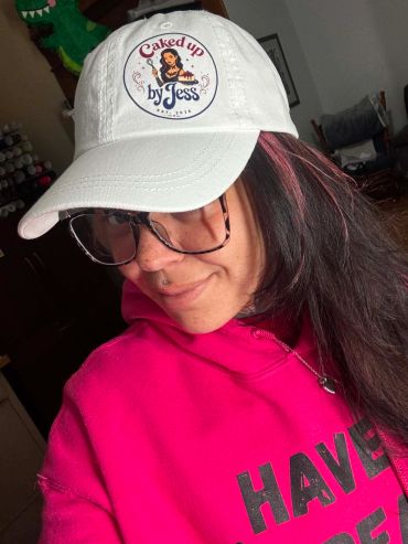 Woman in glasses and white cap with pink hair streaks.