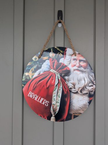 Round Santa sign with red sack hanging on a wall.