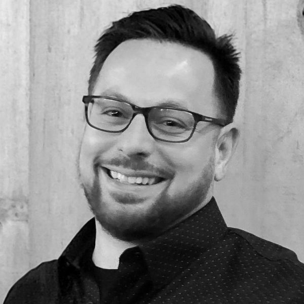 Smiling man with glasses and beard in a black shirt.
