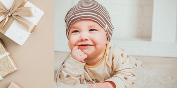 Smiling baby in striped hat lying on soft rug with gifts nearby.