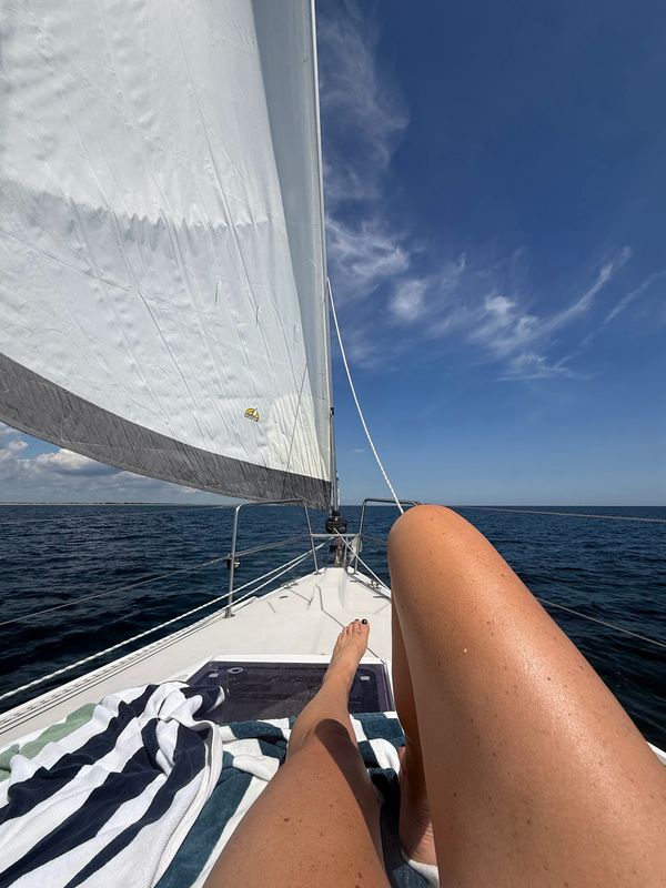 Relaxing legs on a sailboat under clear skies.