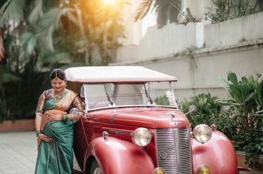 Pregnant woman in traditional attire beside a vintage red car.